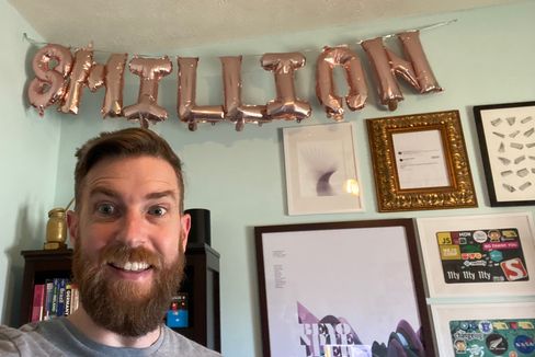 Zach pointing to the new balloons in his office that say 8 Million